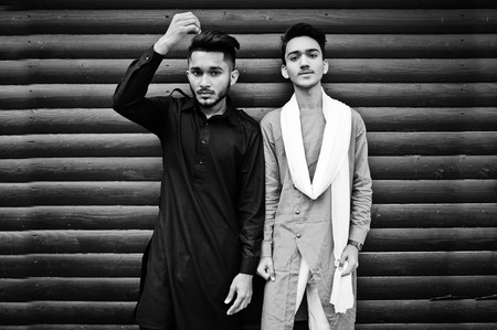 Two indian stylish mans friends in traditional clothes posed outdoor against wooden background.の写真素材