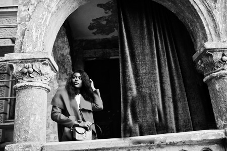 Stylish african american woman in red coat posed against old columns.の写真素材
