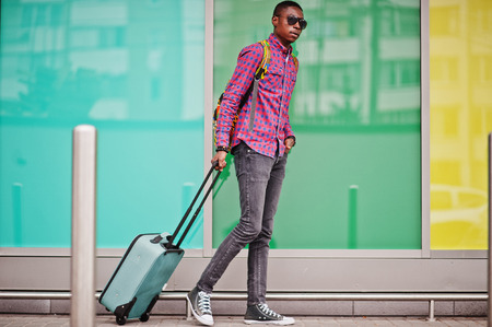 African american man in checkered shirt, sunglasses and jeans with suitcase. Black man traveler.の写真素材