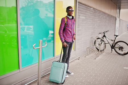 African american man in checkered shirt, sunglasses and jeans with suitcase and backpack. Black man traveler.の写真素材