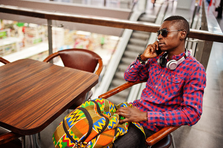 African american man in checkered shirt, sunglasses and jeans with suitcase and backpack. Black man traveler on duty free.の写真素材
