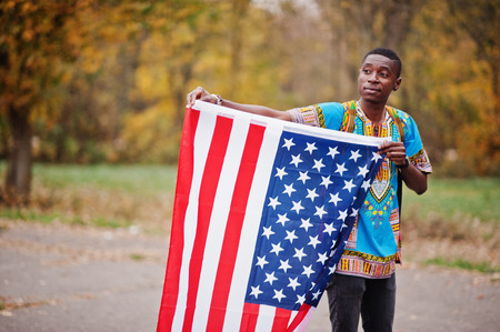 African man in africa traditional shirt on autumn park with USA flag.の写真素材