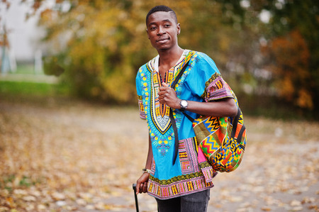 African man in africa traditional shirt on autumn park with backpack and suitcase. Emigrant traveler.の写真素材