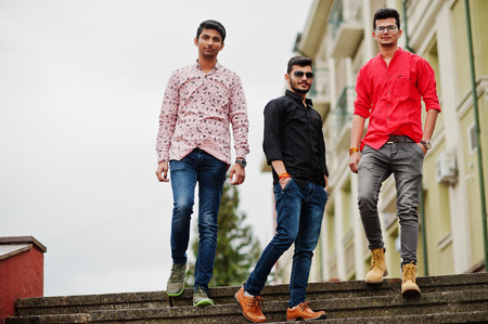 Three indian guys students friends walking on street.