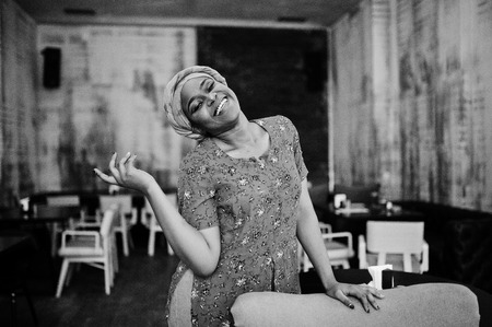 Stylish african woman in red shirt and hat posed indoor cafe.