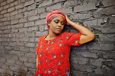 Stylish african woman in red shirt and hat posed against brick wall.