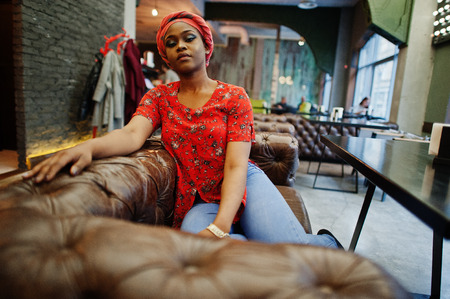 Stylish african woman in red shirt and hat posed indoor cafe.
