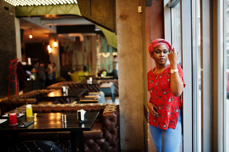 Stylish african woman in red shirt and hat posed indoor cafe.の写真素材