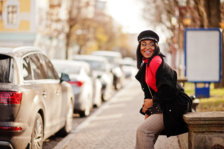 African american fashion girl in coat and newsboy cap posed at street.の写真素材