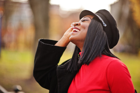 Close up portrait of african american fashion girl in coat and newsboy cap posed at street.