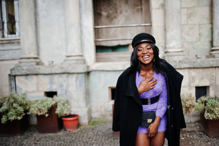 African american woman at violet dress and cap posed outdoor.