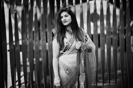 Indian hindu girl at traditional violet saree posed at street against red background.