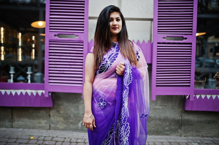 Indian hindu girl at traditional violet saree posed at street against purple windows.