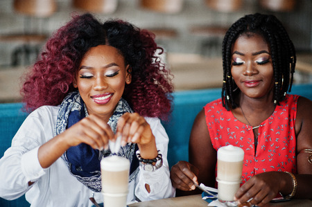 Attractive african american two girls friends sitting at table on cafe with latte.の写真素材