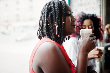 Attractive african american two girls friends sitting at table on cafe with latte.の写真素材