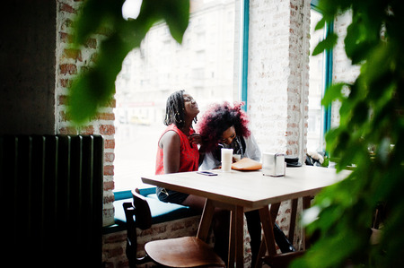 Attractive african american two girls friends sitting at table on cafe with latte.の写真素材