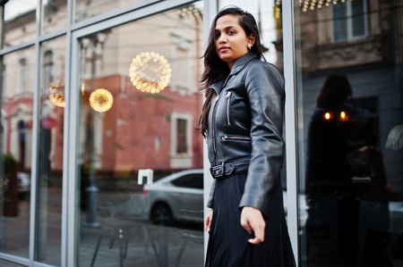 Pretty indian girl in black saree dress and leather jacket posed outdoor at street.