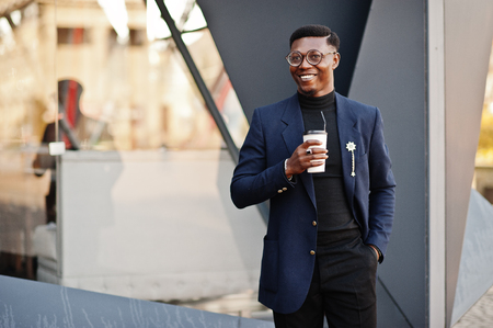 Amazingly looking african american man wear at blue blazer with brooch, black turtleneck and glasses posed at street. Fashionable black guy with cup of coffee.の写真素材