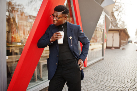 Amazingly looking african american man wear at blue blazer with brooch, black turtleneck and glasses posed at street. Fashionable black guy with cup of coffee.の写真素材