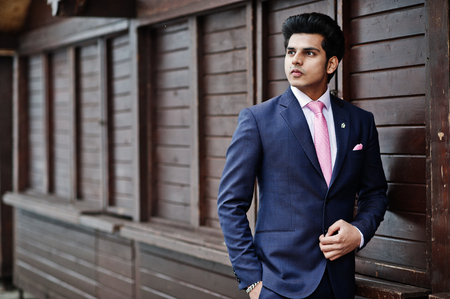 Elegant indian macho man model on suit and pink tie posed against wooden stalls.の写真素材