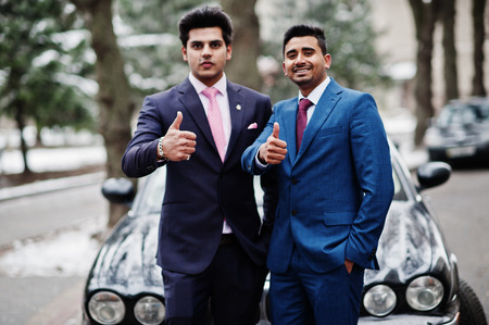Two elegant indian fashionable mans model on suit posed at winter day against black classic car and shows thumbs up.の写真素材