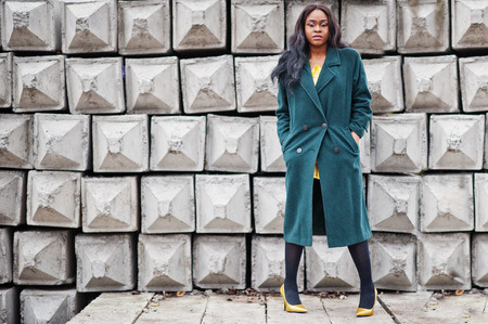 Stylish african american woman at green coat posed against stone texture background.の写真素材