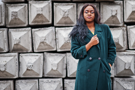 Stylish african american woman at green coat posed against stone texture background.の写真素材