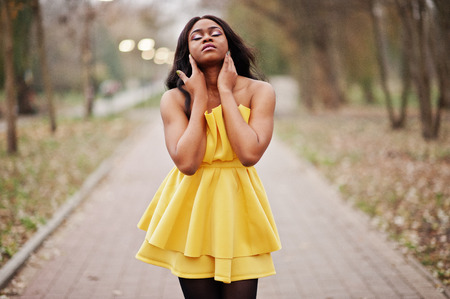 Stylish african american woman at yellow dress posed against autumn park.の写真素材