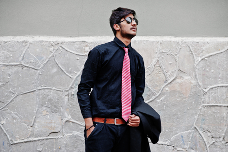 Young indian man on black shirt, tie and sunglasses posed outdoor.の写真素材