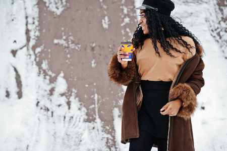 African american woman in sheepskin coat and cap posed at winter day against snowy background with...