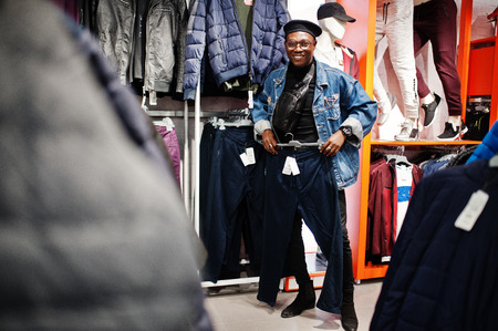 Stylish casual african american man at jeans jacket and black beret at clothes store looking on new...