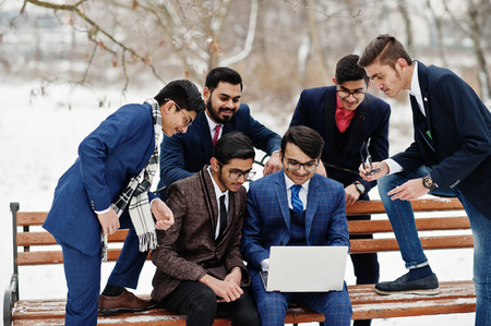 Group of six indian businessman in suits posed outdoor in winter day at Europe, looking on laptop.