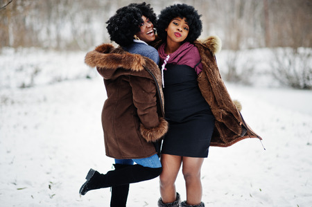 Two curly hair african american woman wear on sheepskin coat and gloves posed at winter day.の写真素材