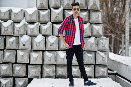 Casual young indian man in checkered shirt and sunglasses posed against stone blocks.の写真素材