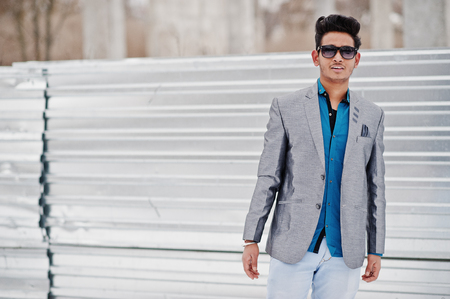 Casual young indian man in silver jacket and sunglasses posed against steelの写真素材