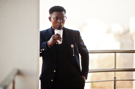 Fashionable african american man in suit and glasses with cup of coffee at hands posed on balkony at office.の写真素材