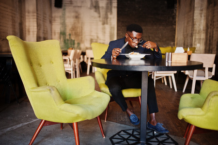 Fashionable african american man in suit and glasses sitting at cafe and eating salad.の写真素材
