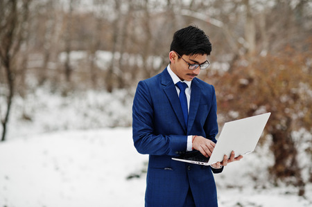 Stylish indian student man in suit and glasses posed at winter day outdoor with laptop at hands.の写真素材