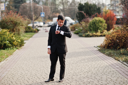 Elegant south asian indian business man in black suit looking at his smart watches on hand.の写真素材