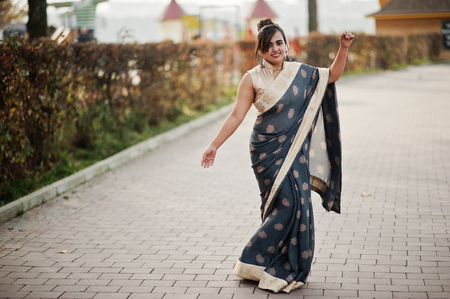 Elegant brunette south asian indian girl in saree dancing outdoor.