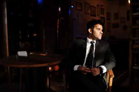 Elegant south asian indian business man in black suit posed indoor cafe in sun shadows.の写真素材