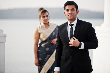 Elegant and fashionable indian friends couple of woman in saree and man in suit posed on the shore of the marina.の写真素材