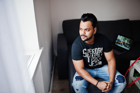 Casual beard indian man sitting at room against laptop.