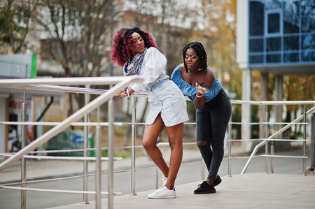 Two attractive african american womans  posed near railings against modern multistory building. Hit on buttocks.の写真素材
