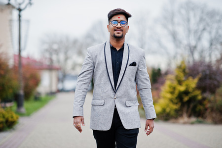 Stylish indian man with bindi on forehead and glasses, wear on suit posed outdoor.