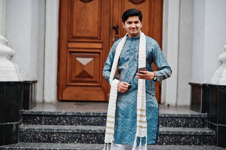 Indian man wear on traditional clothes with white scarf posed outdoor against door of building with mobile phone at  hand.の写真素材