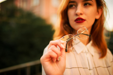 Close up photo of eyeglasses holding redhaired  woman, wear white blouse.の写真素材