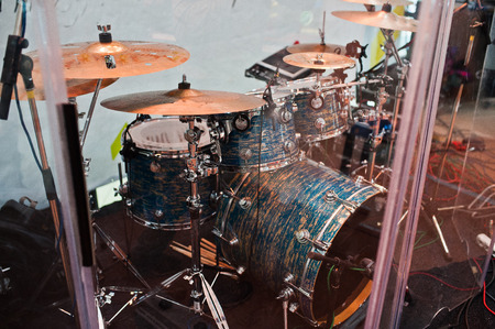 Drum set on stage in a concert hall behing glass wall.