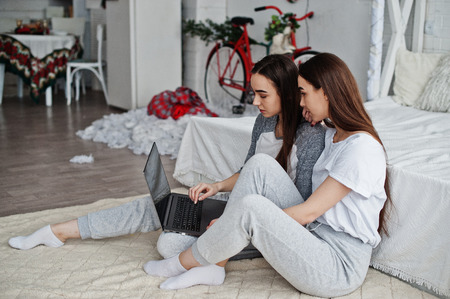 Two twins models with laptop on studio looking something.
