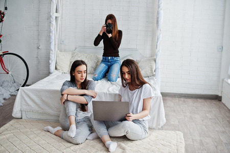 Young girl photographer shooting on studio two twins girls who are watching laptop. Professional...